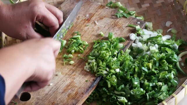 Close up of woman hand cutting up leeks on a wooden chopping board.