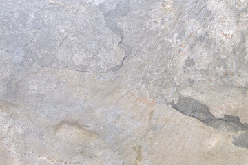 A gray stone wall with a few cracks. The wall is rough and uneven, with some areas looking like they have been chipped away. Scene is somewhat somber and desolate, as the wall appears to be old