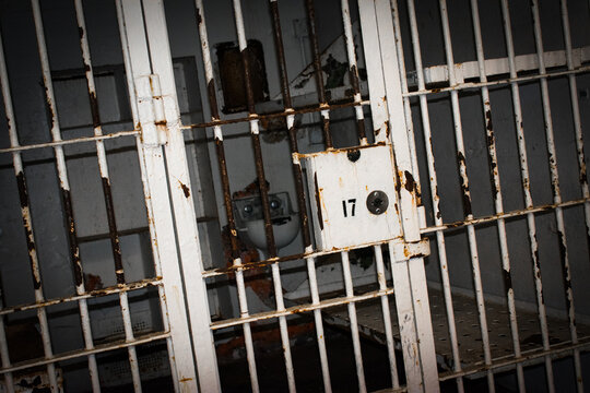 old prison bars showing a prison cell locked with bed and toilet.