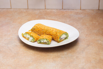 A plate of delicious, homemade carrot rolls filled with creamy ricotta cheese and fresh guacamole, set on a clean, beige kitchen countertop with tiled walls and ample copy space. Healthy homemade food