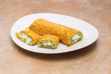 Close-up of an appetizing plate of rolled snacks with a vibrant filling of guacamole and white cheese, wrapped in an orange-hued outer layer of carrot, on a rustic countertop with copy space.