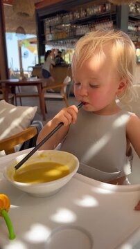 blone toddler girl eating pureed soup through a straw in cafe