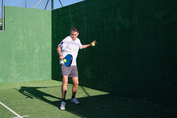 Middle-aged man wearing sportswear is playing paddle tennis on a court, holding a racket and preparing to hit the ball