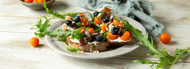 plate with bruschetta with soft cheese and cherry tomatoes on a light table
