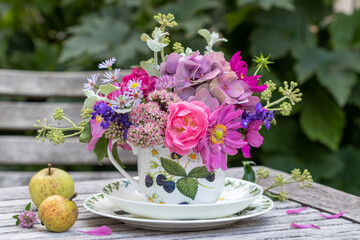 Blumen-Arrangement mit pink und lila Sommerblumen in einer Tasse  im Garten