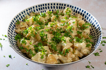 Fresh homemade creamy potato salad, seasoned with finely chopped fresh parsley, made with new baby potatoes of the Gemson variety, served in a large bowl.