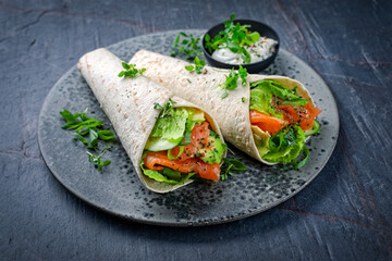 Italian style wrap piada tortilla with cured graved salmon, salad and avocado served as close-up with sour cream dressing dip on a Nordic Design plate