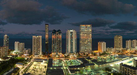 Obraz premium View from above of brightly illuminated high skyscraper buildings in downtown district of Sunny Isles Beach city in Florida, USA. American tourist urban district at night