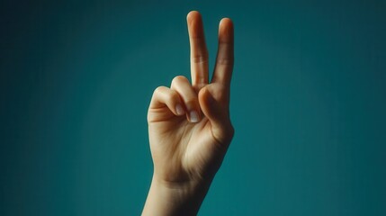 Close-up of a hand making the peace sign against a teal background.
