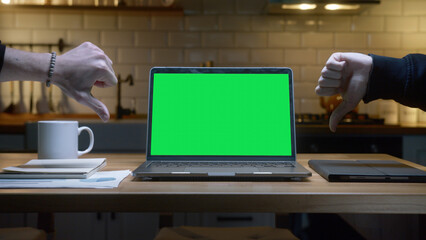 Green screen laptop computer with mock up chromakey display standing on the kitchen table. Anonymous hands showing thumbs down sign background modern kitchen at night