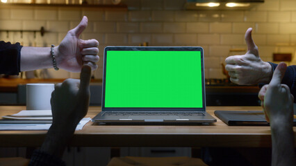 Laptop computer with mock up green screen chromakey display standing on the kitchen table. Anonymous hands showing thumbs up sign background modern kitchen at night