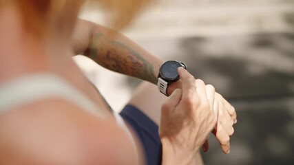 Redhead female athlete checks smart watch at tropical luxury outdoor gym. Pro sportswoman monitors performance, health stats with wearable tech during workout in sunlit fitness space. Slow motion.