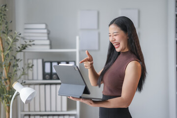 Asian businesswoman is holding a tablet and pointing at it with a happy expression