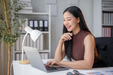 Asian businesswoman is working on a laptop at her desk in an office, she is smiling