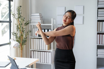Young office manager is relieving muscle tension by stretching her arms while standing in her office