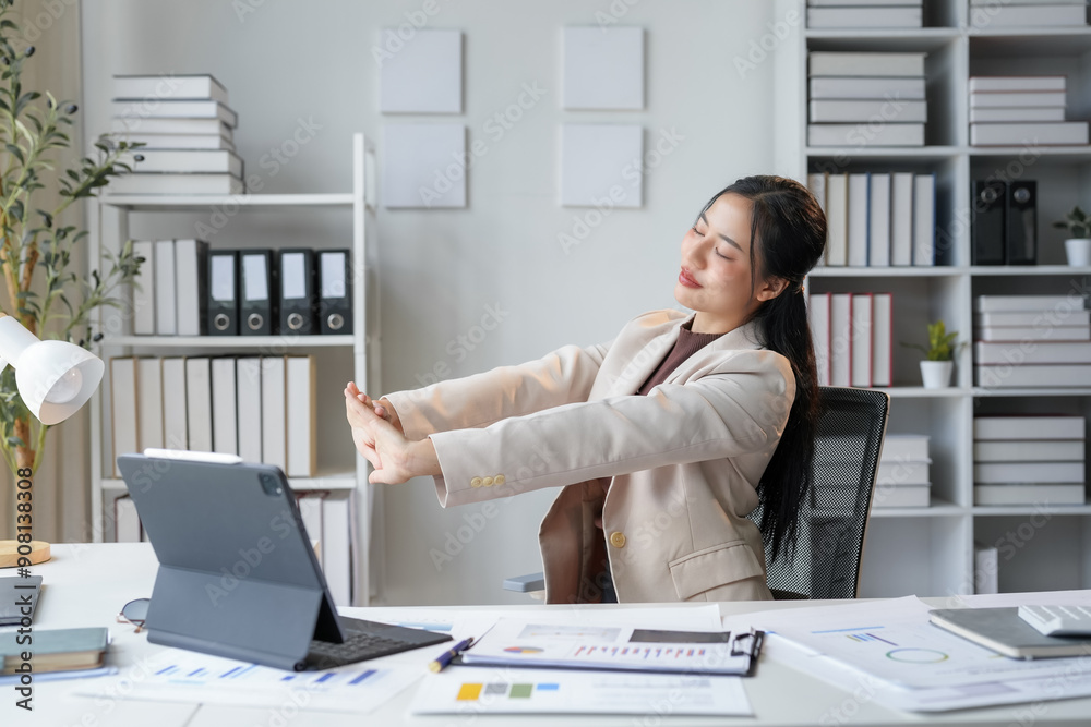 Wall mural businesswoman is relaxing and stretching her arms at her desk in a bright and modern office