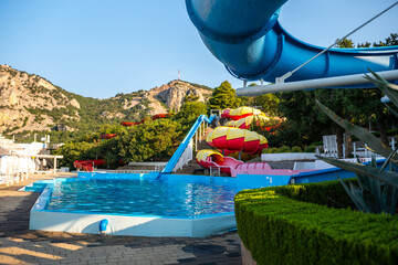 Naklejka premium Water Park Slides Pool Summer - A water park with slides and a pool on a sunny day, surrounded by greenery.