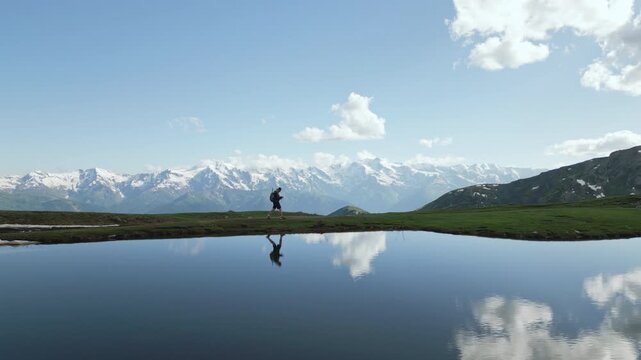 Aerial view of hiker walking by Koruldi lakes in Svaneti mountains. Person backpacking alone in nature. Reflective quiet water, snow-capped peaks, solitude, self reflection, adventure. Drone shot