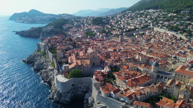Aerial drone film of the historic, ancient walled city of Dubrovnik in Croatia on the Adriatic Sea. Summer colourful city view with defence wall, narrow illuminated streets tiled roofs and fort church