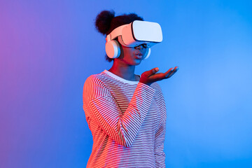 Smiling African woman wearing VR smelling good through metaverse flowers filed world and butterfly insect bug hologram vibrant neon pink blue lighting background technology 3D cyberspace. Contrivance.