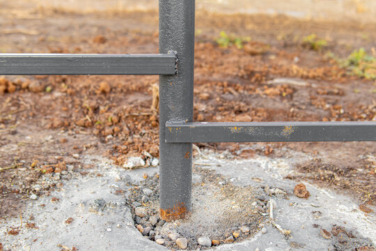 Unfinished dark gray metal fence. Construction of fence on slope. Crossbars welded to an iron post