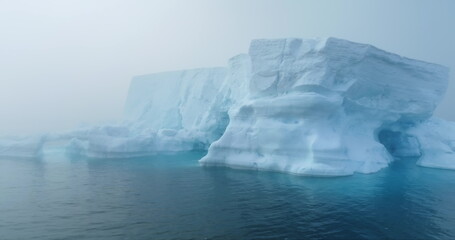 Large iceberg floating in polar ocean in foggy mist day in Antarctica. Tabular huge high ice glacier melting ice cave at wild nature environment. Arctic winter landscape at global warming problem.