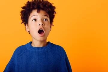 Astonished young african american boy with wide open mouth expressing shock and amazement against a vibrant orange background