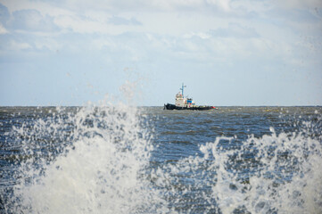 Ship navigates vast ocean with clear sky and crashing waves in foreground