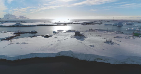 Antarctica polar station buildings on ocean bay coastline. Winter landscape. Snow-covered rocky land. Untouched wilderness of Antarctic nature, mountains in background. Explore, travel to South Pole