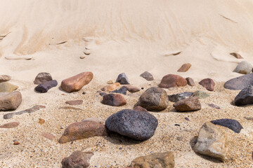 Scattered rocks on sandy beach with dunes in background under clear sky