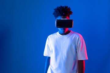 Surprised young African American looking through VR holding interesting object hologram on pink...