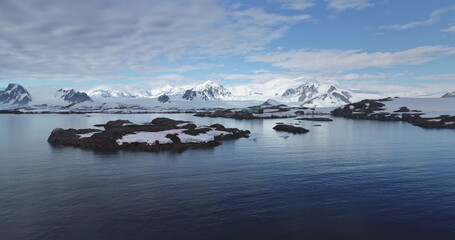 Antarctic polar station on rocky ocean cost, towering snow covered mountains under blue sky. Science research base on South Pole. Antarctica travel and exploration, expeditions. Aerial drone flight