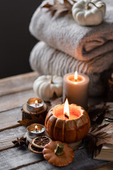 Cozy fall table decoration for Thanksgiving, romantic autumn home composition with small pumpkins, candles, wooden knitted sweater, book, dry leaves. Countryside rustic style
