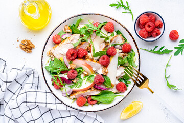 Delicious summer salad with raspberries, chicken meat, fresh pears, ricotta cheese, red onion, nuts, spinach and arugula, white background, top view