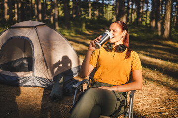 Obraz premium young woman sit in front tent and drink coffee in a thermos