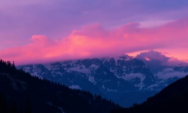 Pink Skies Over Majestic Peaks: A breathtaking panorama of snow-capped mountains bathed in the ethereal glow of a vibrant pink sunset, evoking a sense of awe and wonder. The clouds cast a dramatic sil