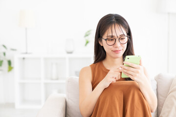 部屋でスマホを見る若い女性