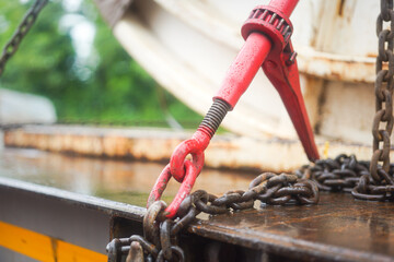 Steel chain and hook securing anchor, using to secure heavy object that transported on the trailer truck. Industrial safety equipment, close-up at the object.