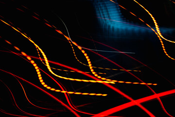 The image is a blurry, abstract representation of a car's headlights. The red and orange lines create a sense of movement and energy, while the black background adds a sense of depth and contrast