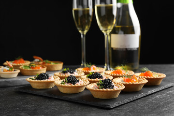 Delicious canapes with salmon and caviar on black textured table, closeup