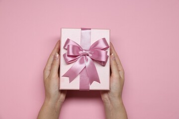 Woman holding gift box with bow on pink background, top view