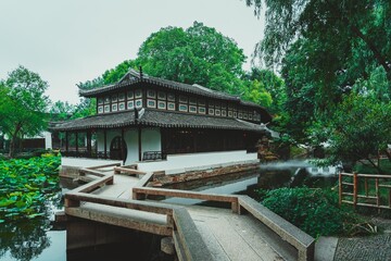 A traditional Chinese garden in Suzhou, with a white building, a stone bridge, and a pond with lily...