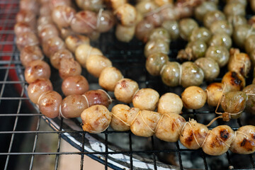 Handmade Thai sausage balls baking on a gridiron grill and ready for sell.