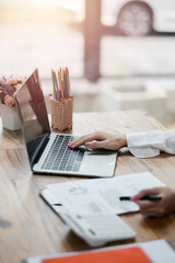 Close-up of a business professional using a laptop and reviewing documents with a calculator on a...