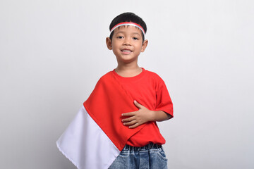 Asian boy smiling happily with Indonesian flag draped over his shoulder, isolated on white background. Indonesian Independence Day concept.