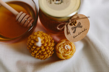 Organic honey in a glass jar and a glass small bowl and burning candles made of natural handmade wax on a white background. Beekeeping products. Small business. Farm.
