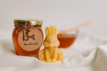 Organic honey in a glass jar and a glass small bowl and burning candles made of natural handmade wax on a white background. Beekeeping products. Small business. Farm.