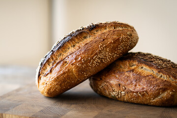 Two loaves of sourdough bread, freshly baked and still warm, are stacked on a wooden surface. The...