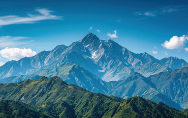 Fototapeta premium Breathtaking view of a majestic mountain range under a clear blue sky with lush green hills in the foreground.