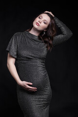 Portrait of young pregnant female in grey sequin dress with hands near pregnant belly.